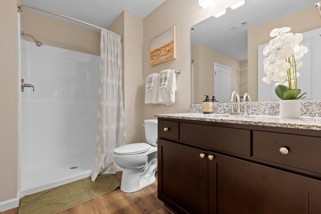 Modern bathroom with a walk-in shower, toilet, granite countertop vanity with sink, white towels, and a potted orchid on the counter.