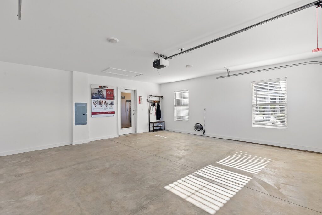 A clean, empty garage with white walls, two windows, a concrete floor, and some wall-mounted items including a calendar and coat hooks.
