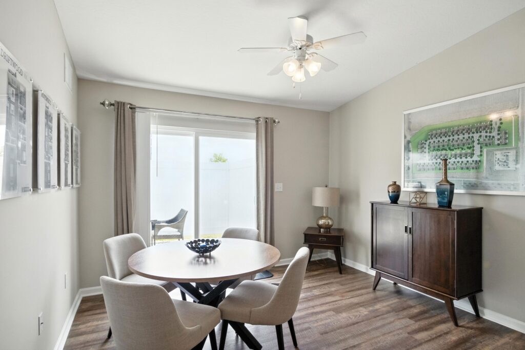 A dining area with a round table and four chairs, wall art, a ceiling fan, a sideboard with decor, and sliding glass doors with curtains letting in natural light.