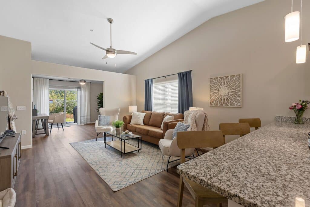 Open-concept living room and kitchen with modern furnishings, granite countertops, wood flooring, and large windows letting in natural light.