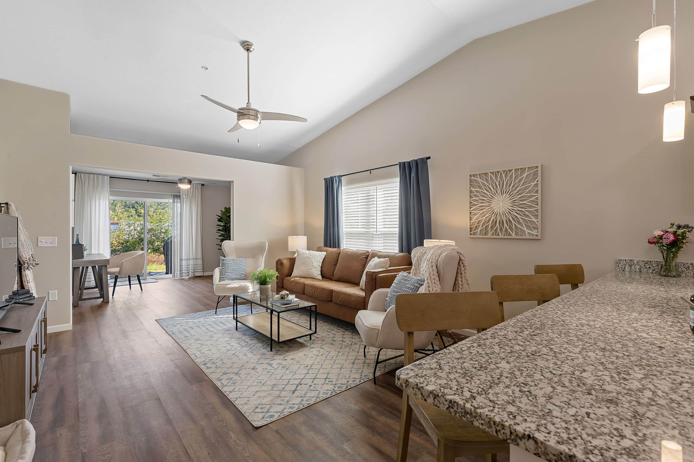 Open-concept living room and kitchen with modern furnishings, granite countertops, wood flooring, and large windows letting in natural light.