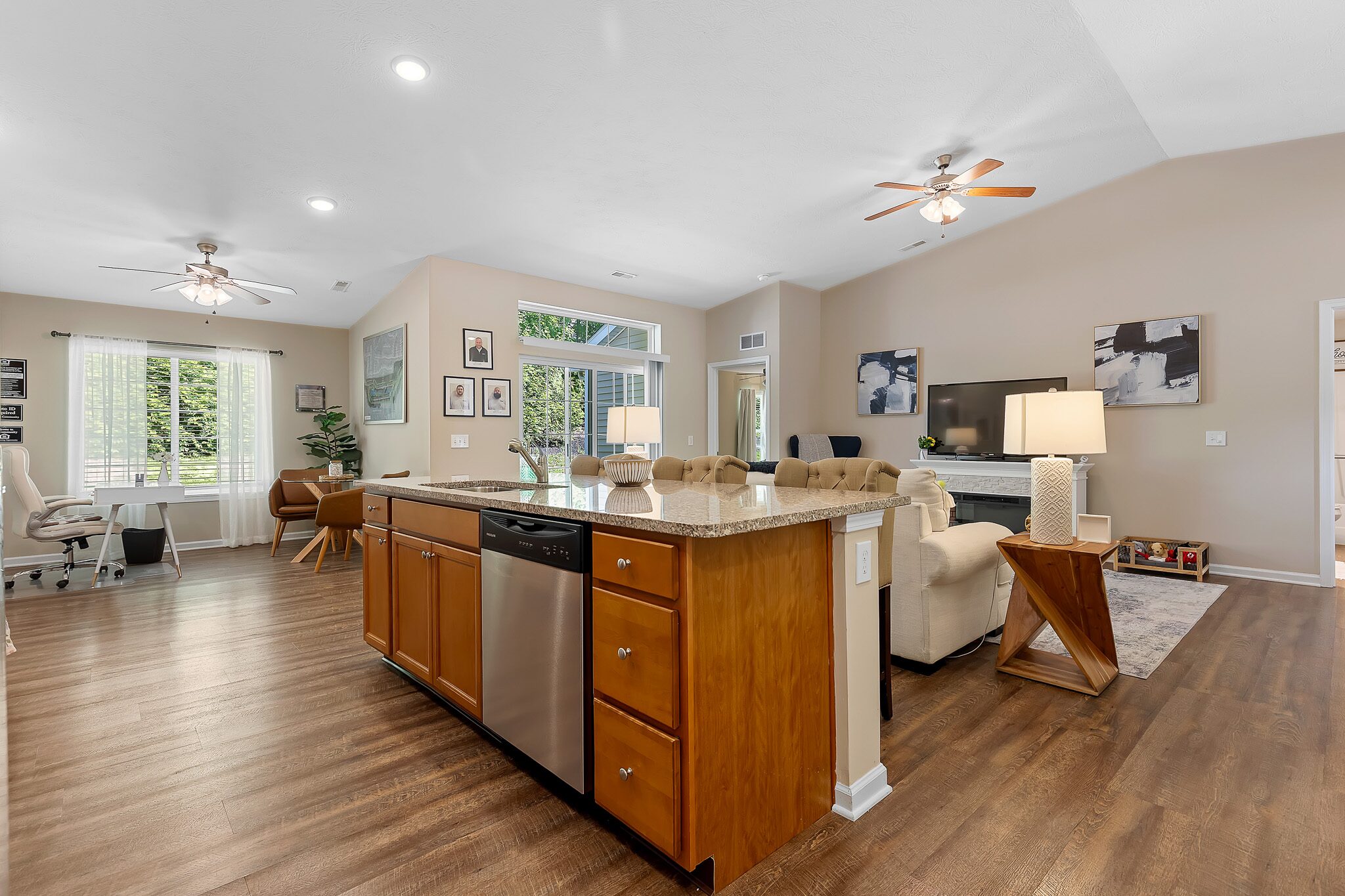 Open-concept living space with a kitchen island, stainless steel appliances, dining area, and living room featuring wood floors, neutral walls, and ceiling fans.