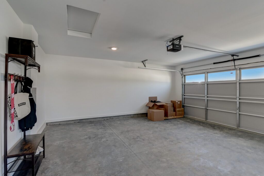 Clean, empty garage with concrete floor, metal shelves on the left holding some bags and jackets, and several cardboard boxes stacked near the closed garage door.