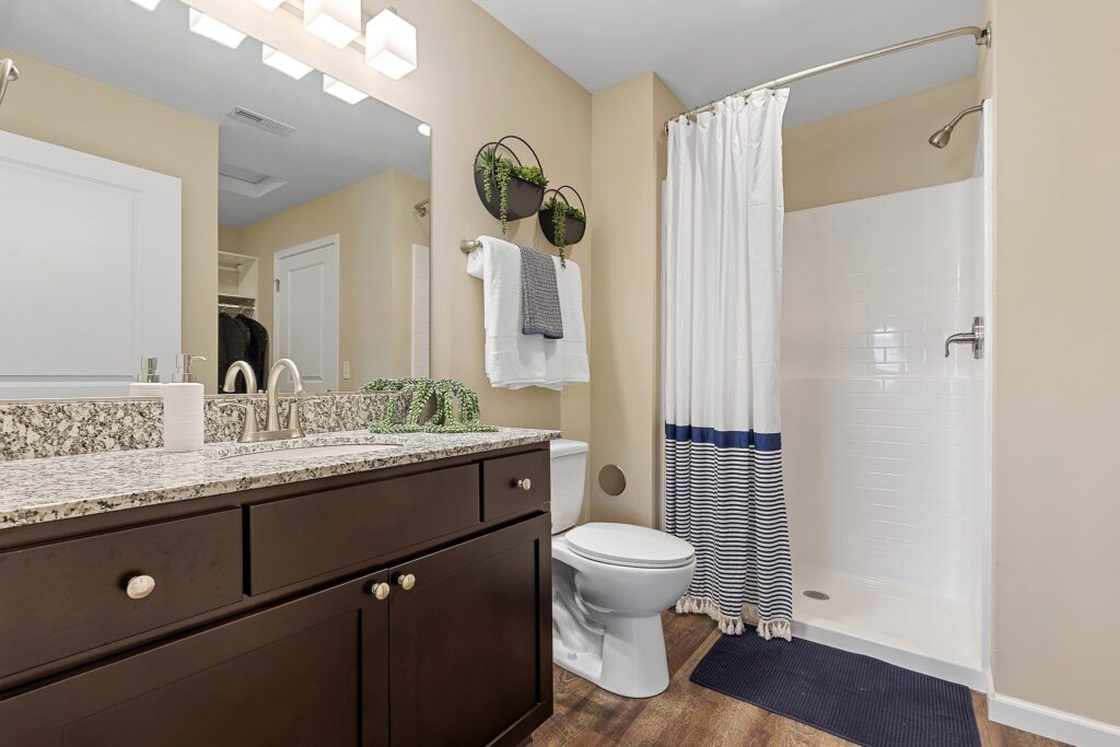 Modern bathroom with granite countertop, double sink, toilet, walk-in shower with striped curtain, towel racks, mirror, and wall-mounted planters.