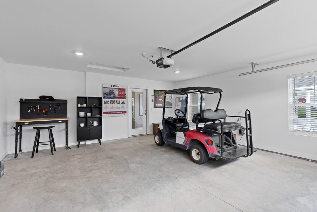 A clean garage with a red golf cart parked inside, a small black workbench with tools, shelving, and posters on the wall.