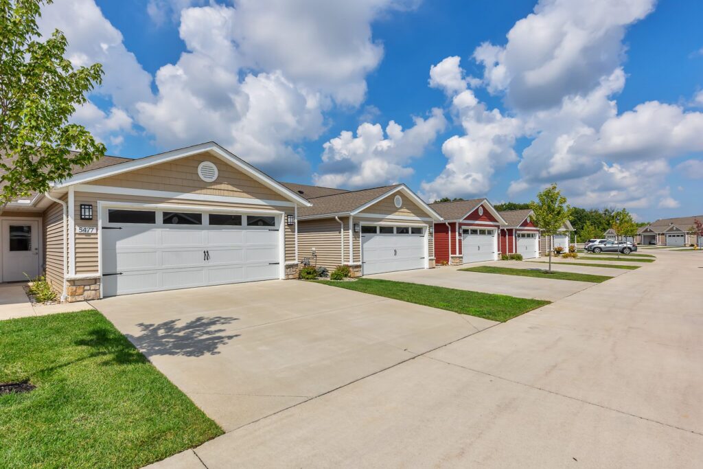 Row of single-story suburban houses with attached garages and driveways under a partly cloudy sky.
