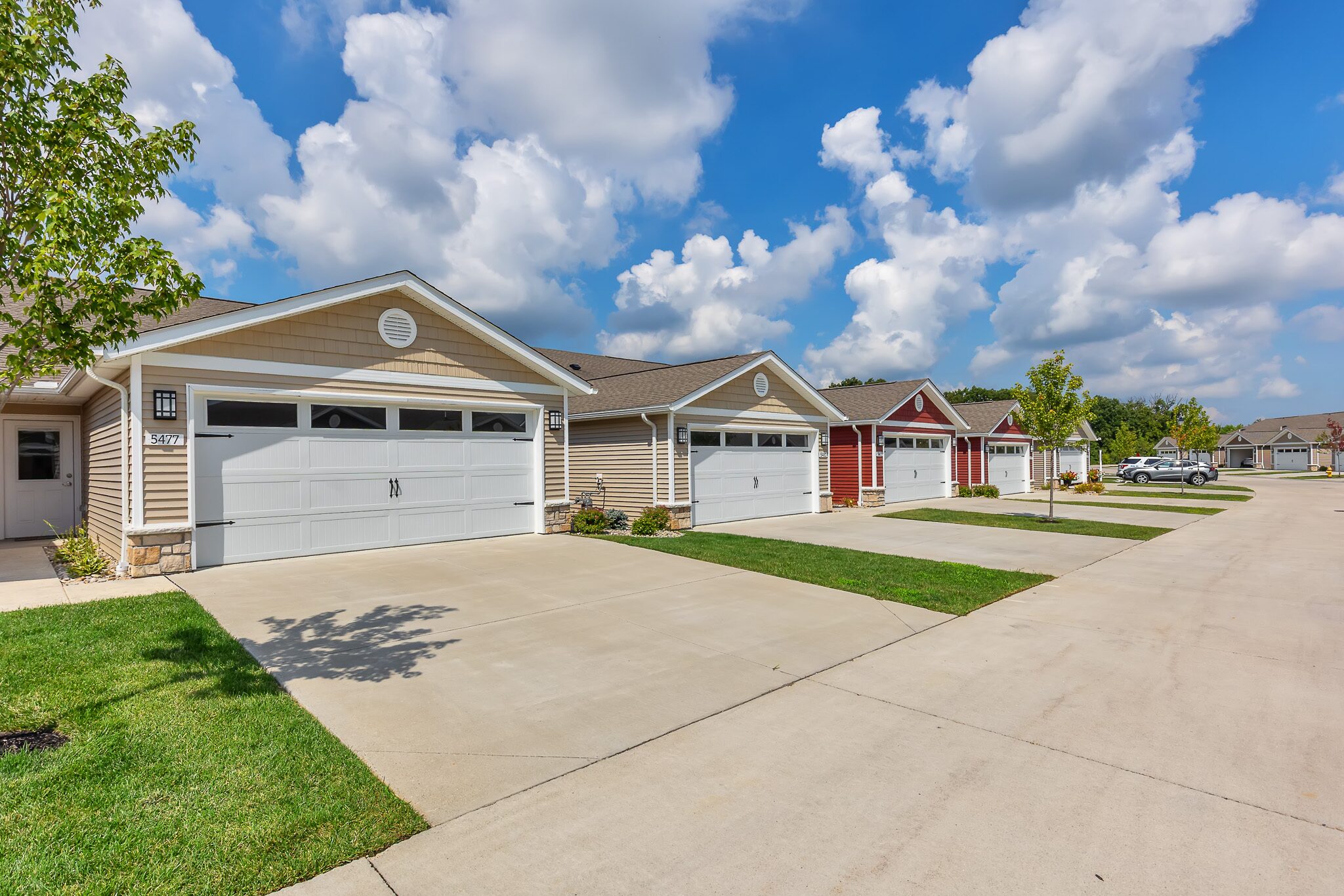 Row of single-story suburban houses with attached garages and driveways under a partly cloudy sky.