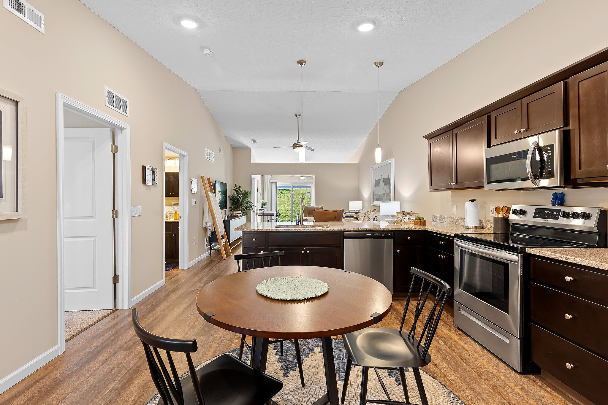 Modern kitchen and dining area with dark wood cabinets, stainless steel appliances, round dining table with four chairs, and light beige walls.