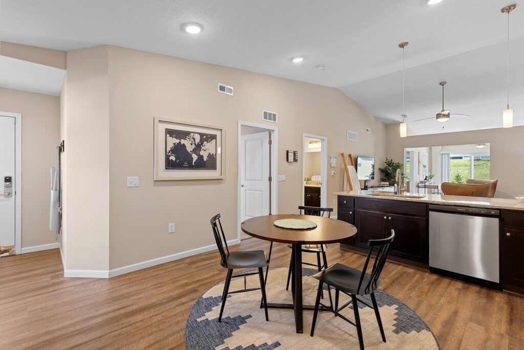 Open-concept dining and kitchen area with a round table and three chairs, dark wood cabinets, pendant lights, and a wall map artwork.