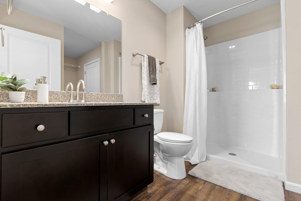 Modern bathroom with a dark wood vanity, granite countertop, toilet, white tile shower with curtain, and a towel hanging on the wall.