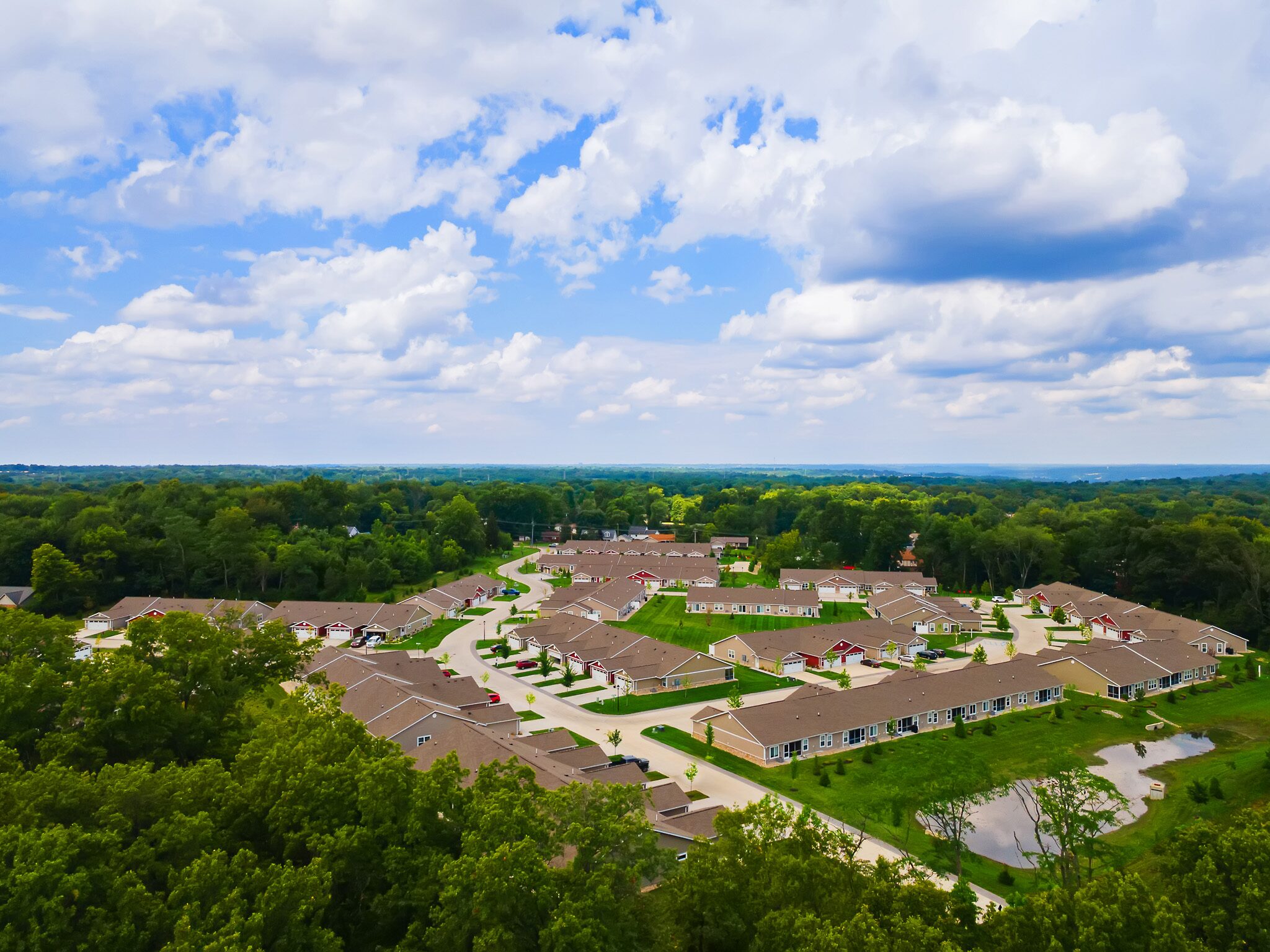 Aerial view of a suburban residential neighborhood surrounded by trees under a partly cloudy sky.