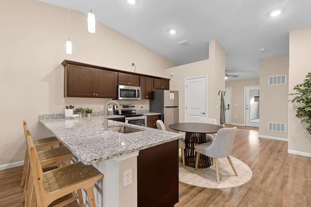 Modern kitchen and dining area with granite countertops, wood cabinets, stainless steel appliances, round dining table, and light wood flooring.