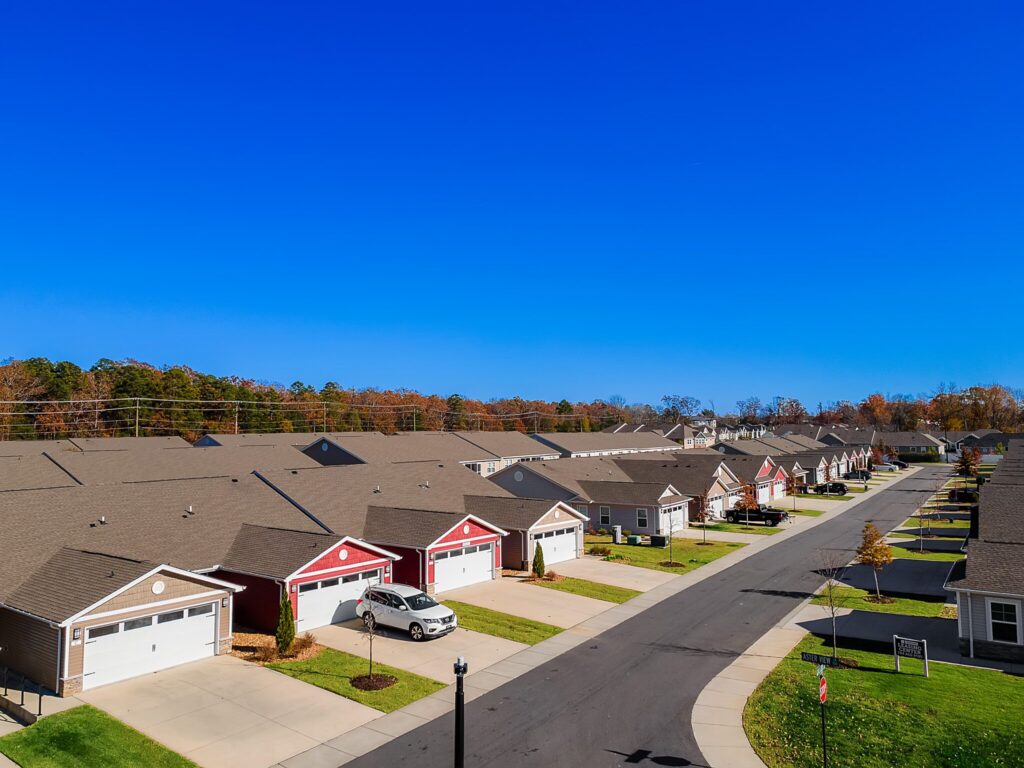 Aerial view of a suburban neighborhood with rows of single-story houses, driveways, and a clear blue sky.