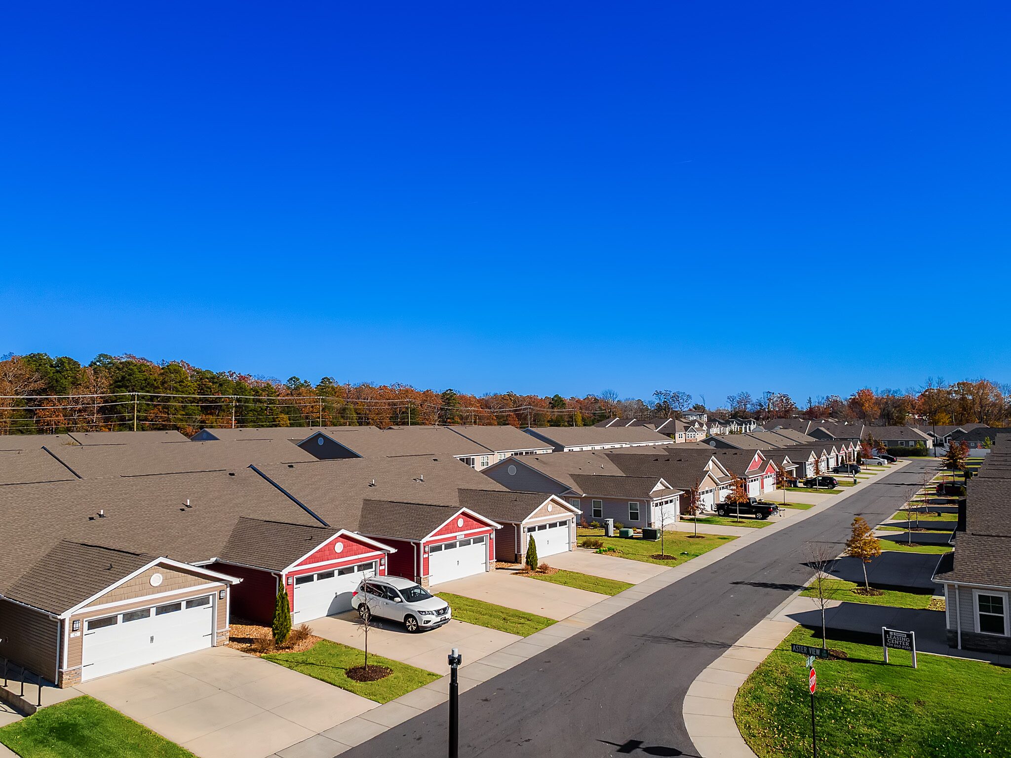 Aerial view of a suburban neighborhood with rows of single-story houses, driveways, and a clear blue sky.