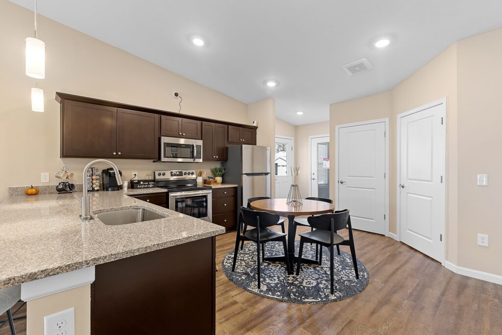 Modern kitchen with dark cabinets, granite countertops, stainless steel appliances, and a round dining table with four chairs on a patterned rug.