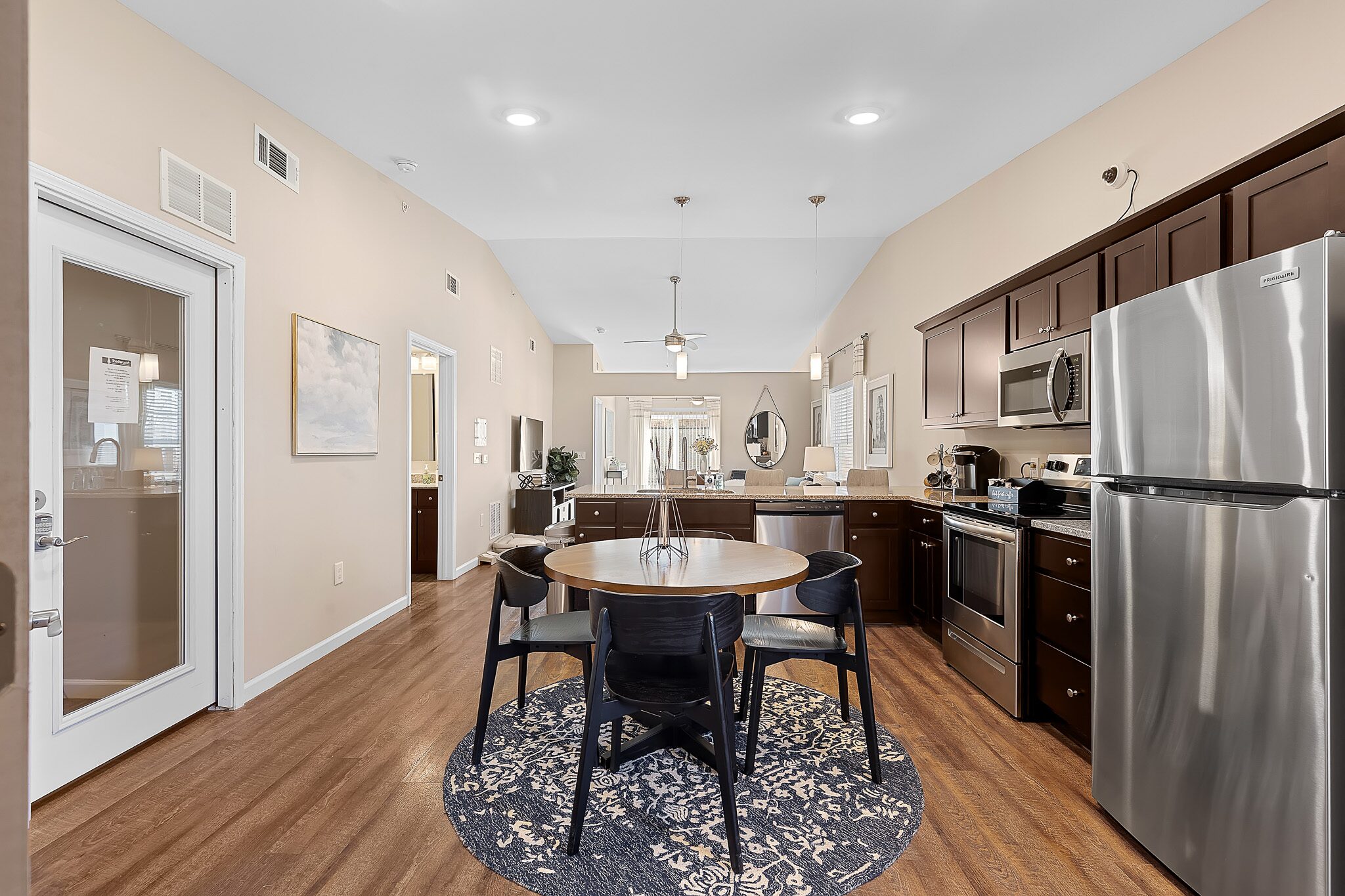 Modern kitchen and dining area with stainless steel appliances, dark wood cabinets, a round dining table with four chairs, and wood flooring.