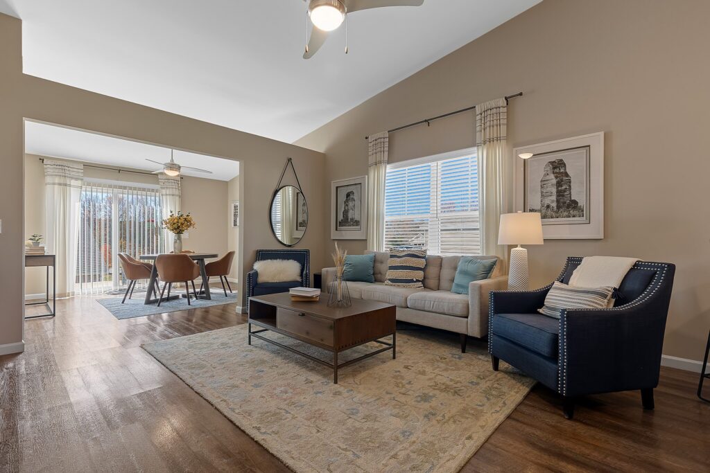 A modern living room with a beige sofa, two dark blue armchairs, a wooden coffee table, and a dining area in the background with a table and six chairs.