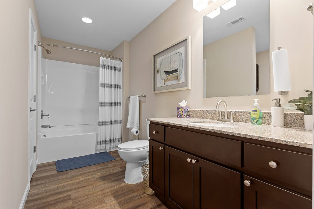 Modern bathroom with a dark wood vanity, granite countertop, toilet, bathtub with shower, striped shower curtain, and wall art above the towel rack.