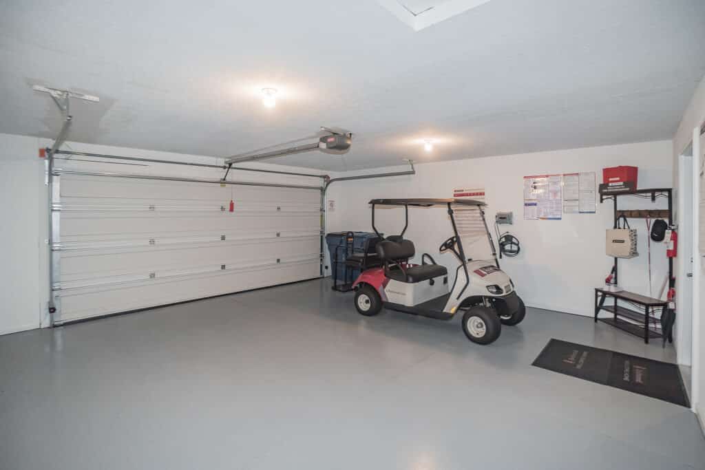 A clean, spacious garage with a golf cart, storage bins, wall hooks, a shelf, and a large closed garage door.