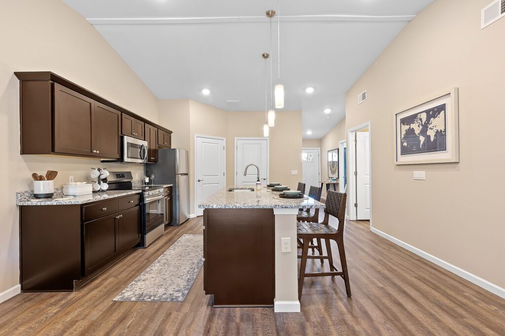 Modern kitchen with dark wood cabinets, stainless steel appliances, granite island with barstools, pendant lighting, and a world map artwork on the wall.