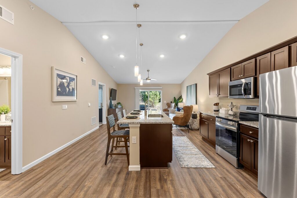 Modern open-concept kitchen and living area with stainless steel appliances, dark wood cabinets, island with barstools, and sliding doors leading to a patio.