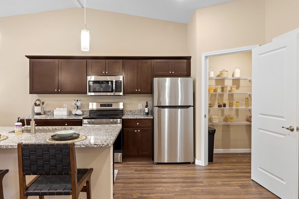 Modern kitchen with dark wood cabinets, stainless steel appliances, granite countertops, and an open pantry stocked with jars and containers.