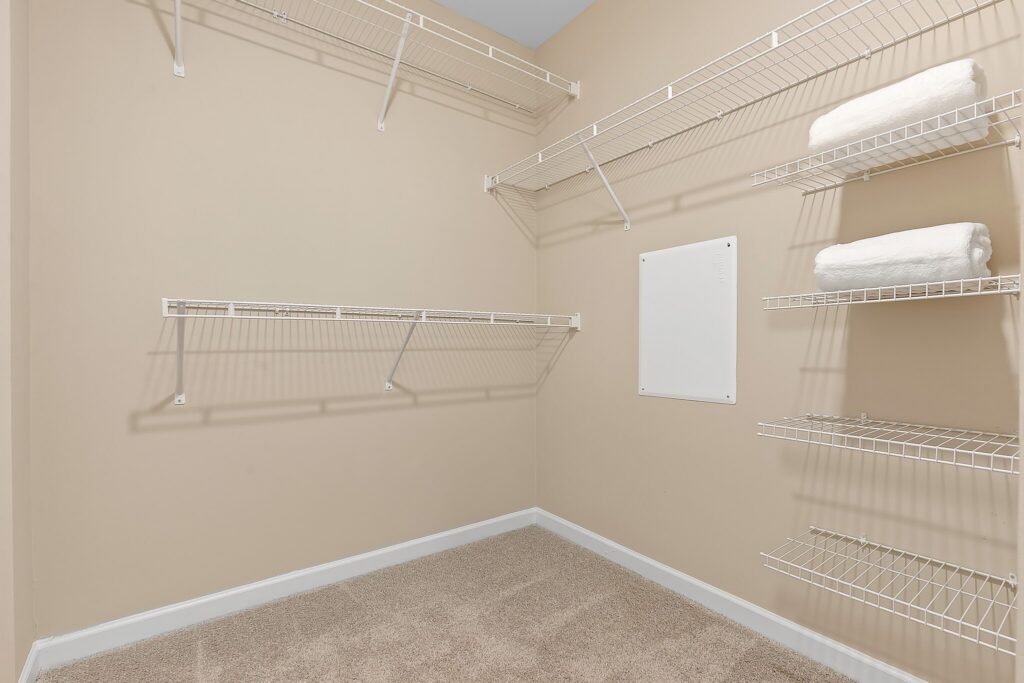 Empty walk-in closet with beige walls, carpeted floor, and white wire shelving; two white towels folded on one of the shelves.