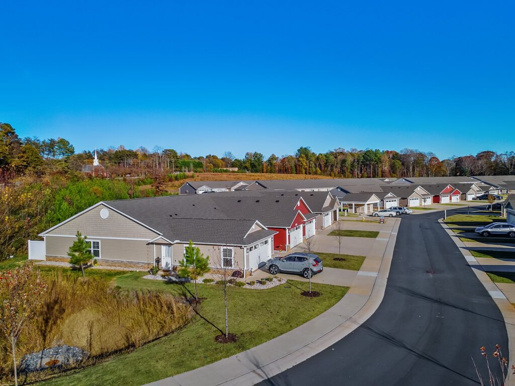 A row of single-story townhouses with driveways and cars, lining a clean, paved street in a suburban neighborhood on a clear day.