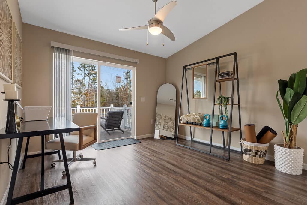 Modern home office with a desk and chair, large mirror, decorative shelving, potted plant, and sliding glass doors leading to a patio.