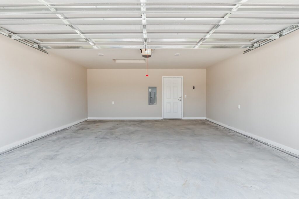 Empty two-car garage with a concrete floor, white walls, a closed side door, and an open garage door overhead.