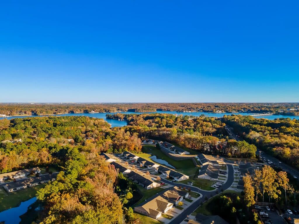 Aerial view of a suburban neighborhood surrounded by trees and several lakes under a clear blue sky.