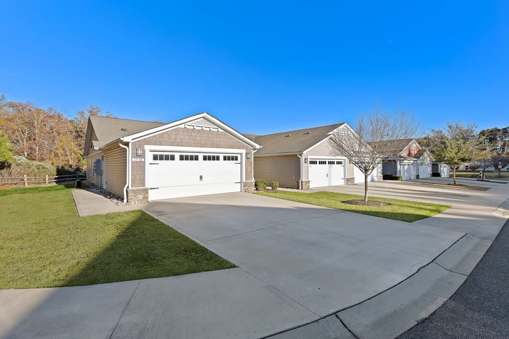 Two single-story suburban houses with attached garages, concrete driveways, and a small front lawn on a clear, sunny day.