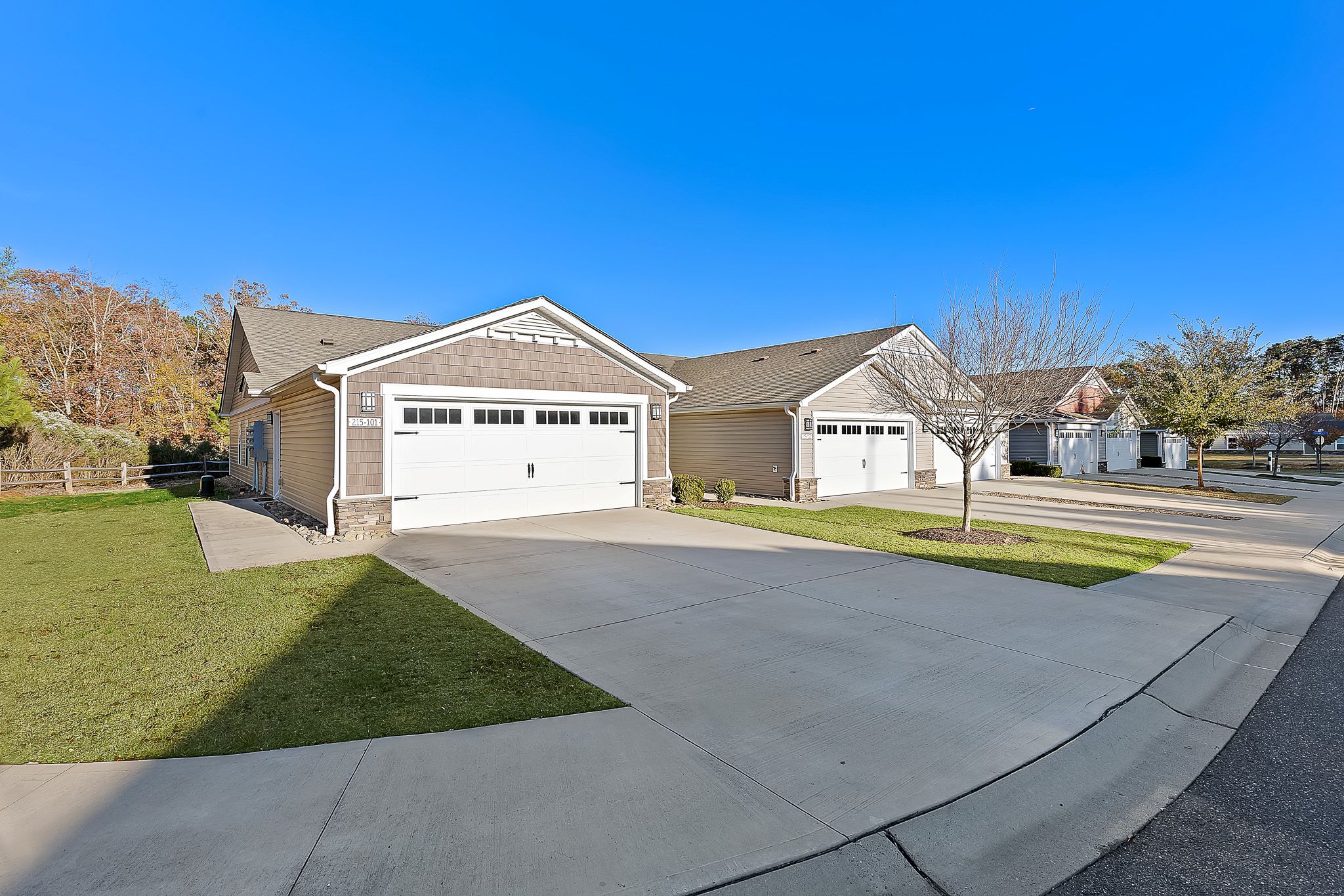 Two single-story suburban houses with attached garages, concrete driveways, and a small front lawn on a clear, sunny day.