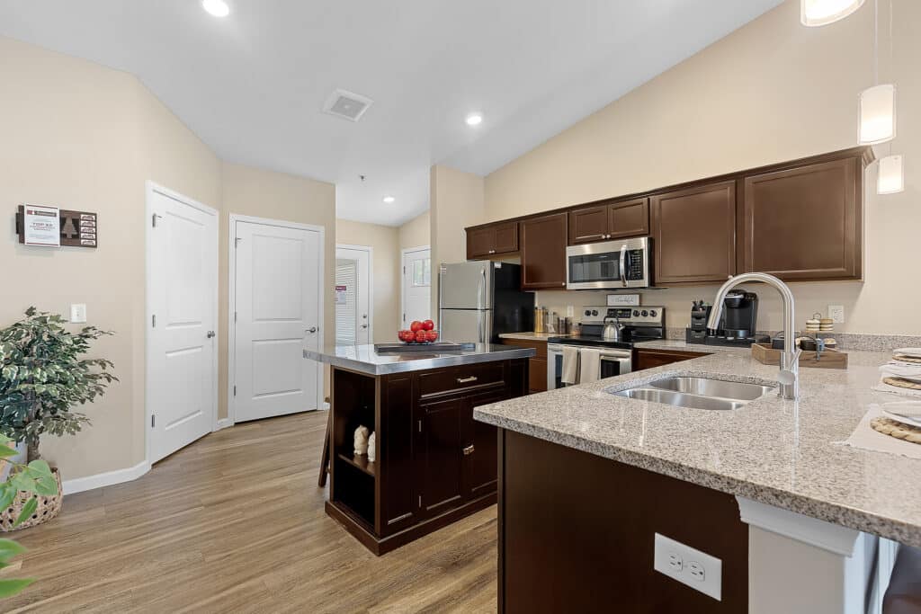 Modern kitchen with dark wood cabinets, stainless steel appliances, granite countertops, center island, and wood flooring. Three pendant lights hang above the counter.