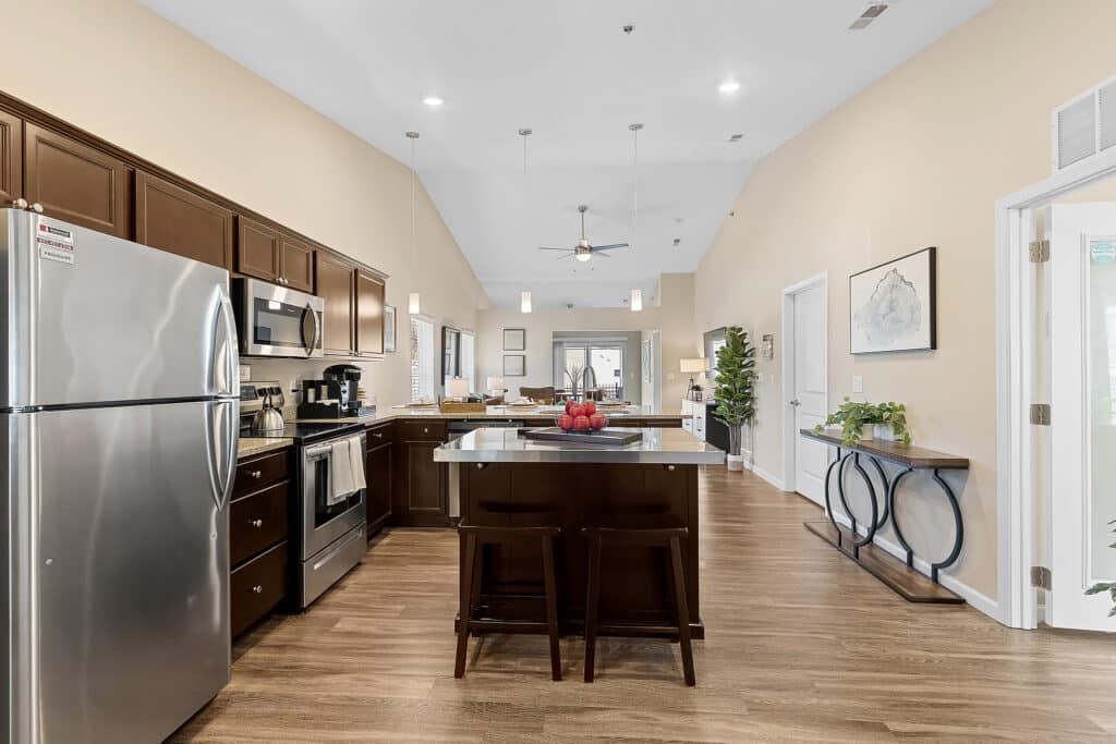 Modern kitchen with stainless steel appliances, dark wood cabinets, center island with stools, and light wood flooring in an open-concept living space.