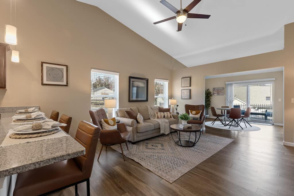Open-concept living and dining area with wood flooring, beige walls, modern furniture, a ceiling fan, and large windows letting in natural light.