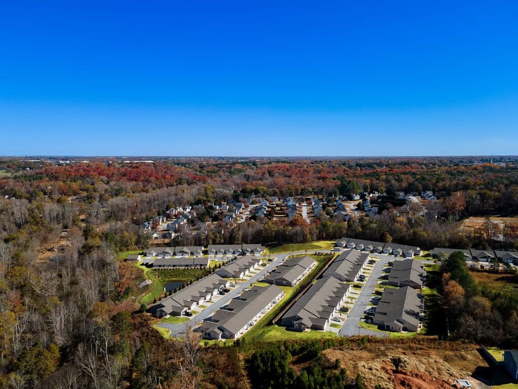 Aerial view of a residential neighborhood with rows of houses surrounded by trees and a clear blue sky.
