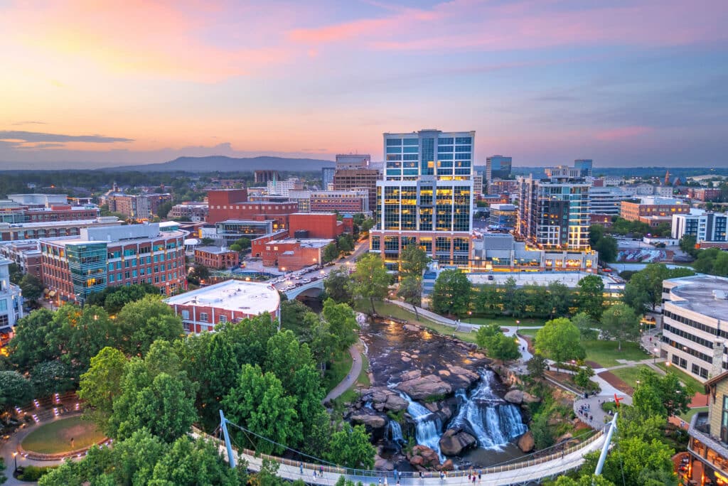 A cityscape at sunset shows modern buildings, a river with waterfalls, and green parks in the foreground under a pastel sky.