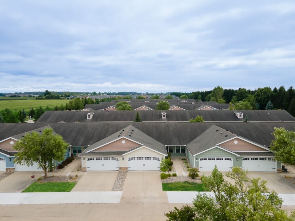 Aerial view of a row of suburban townhouses with attached garages, surrounded by trees and greenery under a cloudy sky.