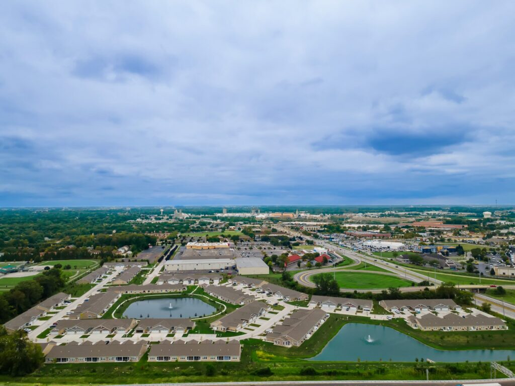 Aerial view of a suburban neighborhood with ponds, roads, and commercial buildings under a cloudy sky.