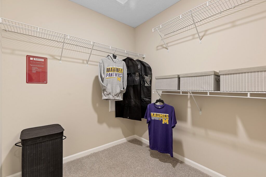 Walk-in closet with wire shelving, two storage bins, a laundry hamper, and two Maumee Panthers shirts hanging on hangers.