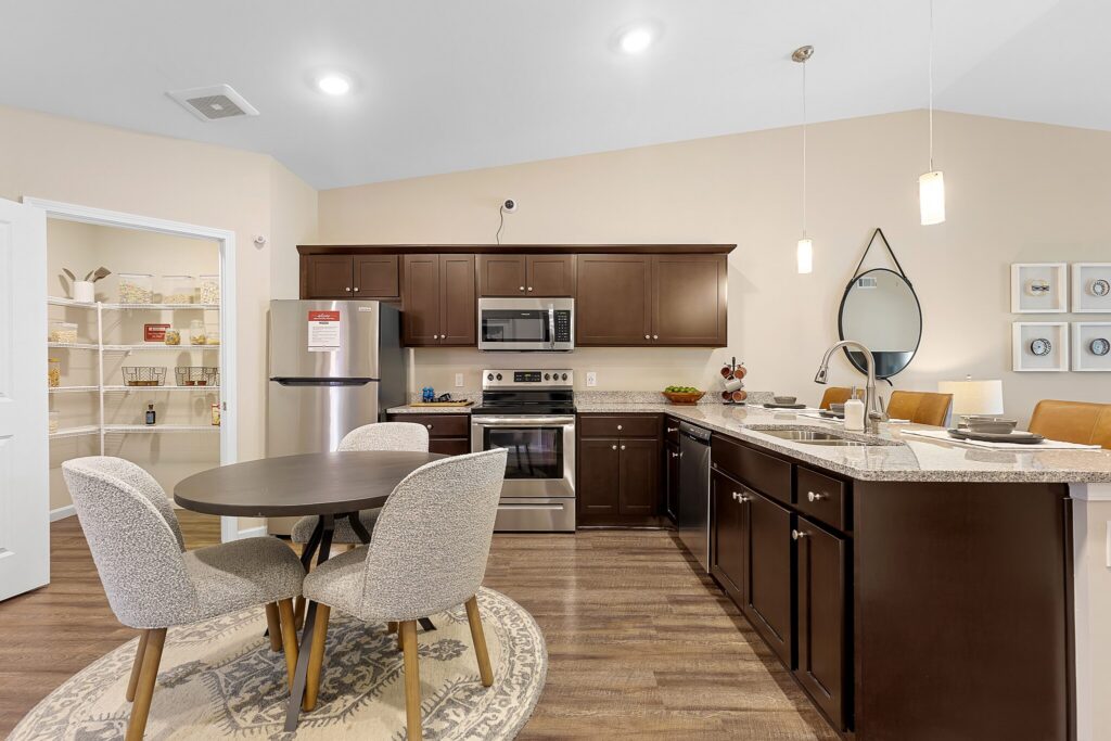 Modern kitchen with dark wood cabinets, stainless steel appliances, a round dining table with four chairs, and a large pantry with open shelving.