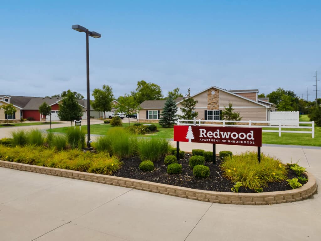A landscaped entrance with a sign reading "Redwood Apartment Neighborhoods" in front of single-story residential buildings.