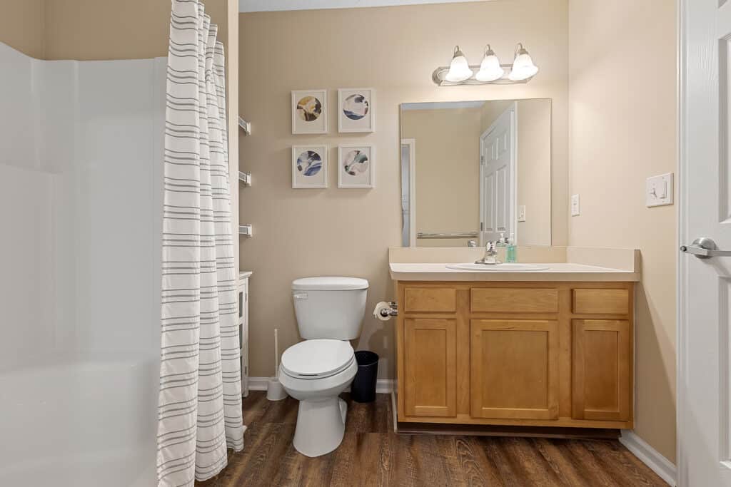 Bathroom with a shower and striped curtain, toilet, wooden vanity with sink, mirror, wall art, and overhead light fixture.