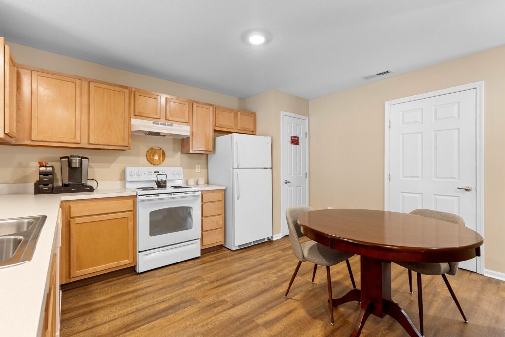 A kitchen with wooden cabinets, white appliances, a round dining table with four chairs, and a wood-style floor.