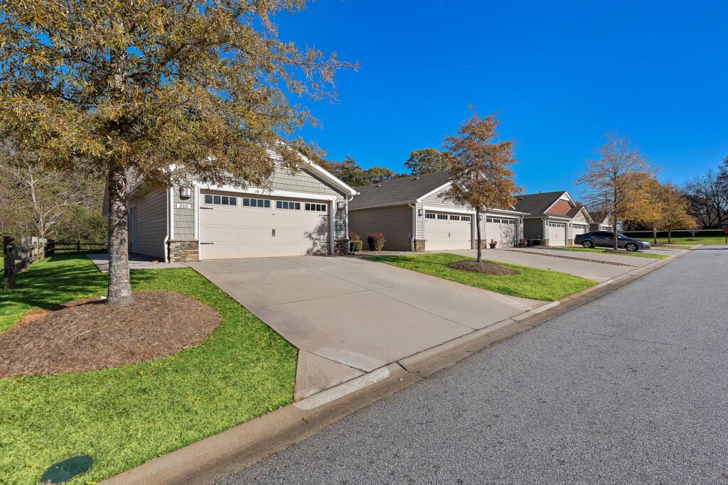 Row of suburban single-story houses with attached garages, concrete driveways, and small front lawns on a clear, sunny day.