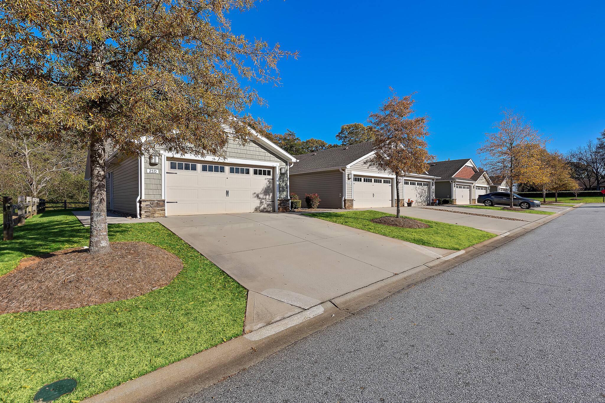 Row of suburban single-story houses with attached garages, concrete driveways, and small front lawns on a clear, sunny day.