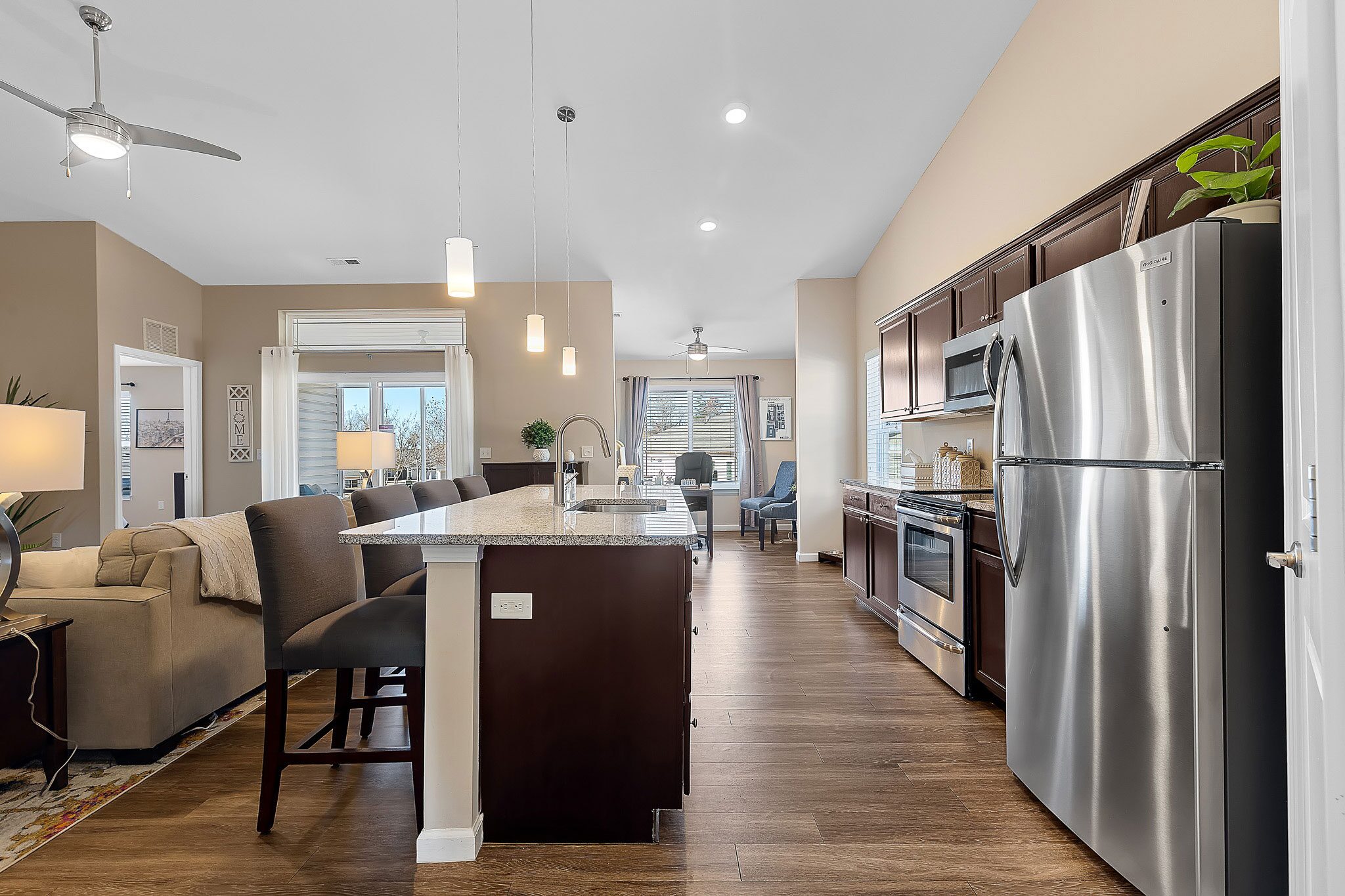 Modern open-concept kitchen and living area with stainless steel appliances, dark wood cabinets, island seating, and large windows letting in natural light.