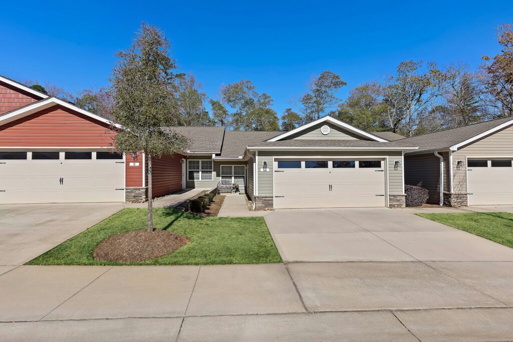 Single-story suburban house with beige siding, a double garage, and a small front yard, situated between two similar houses on a sunny day.
