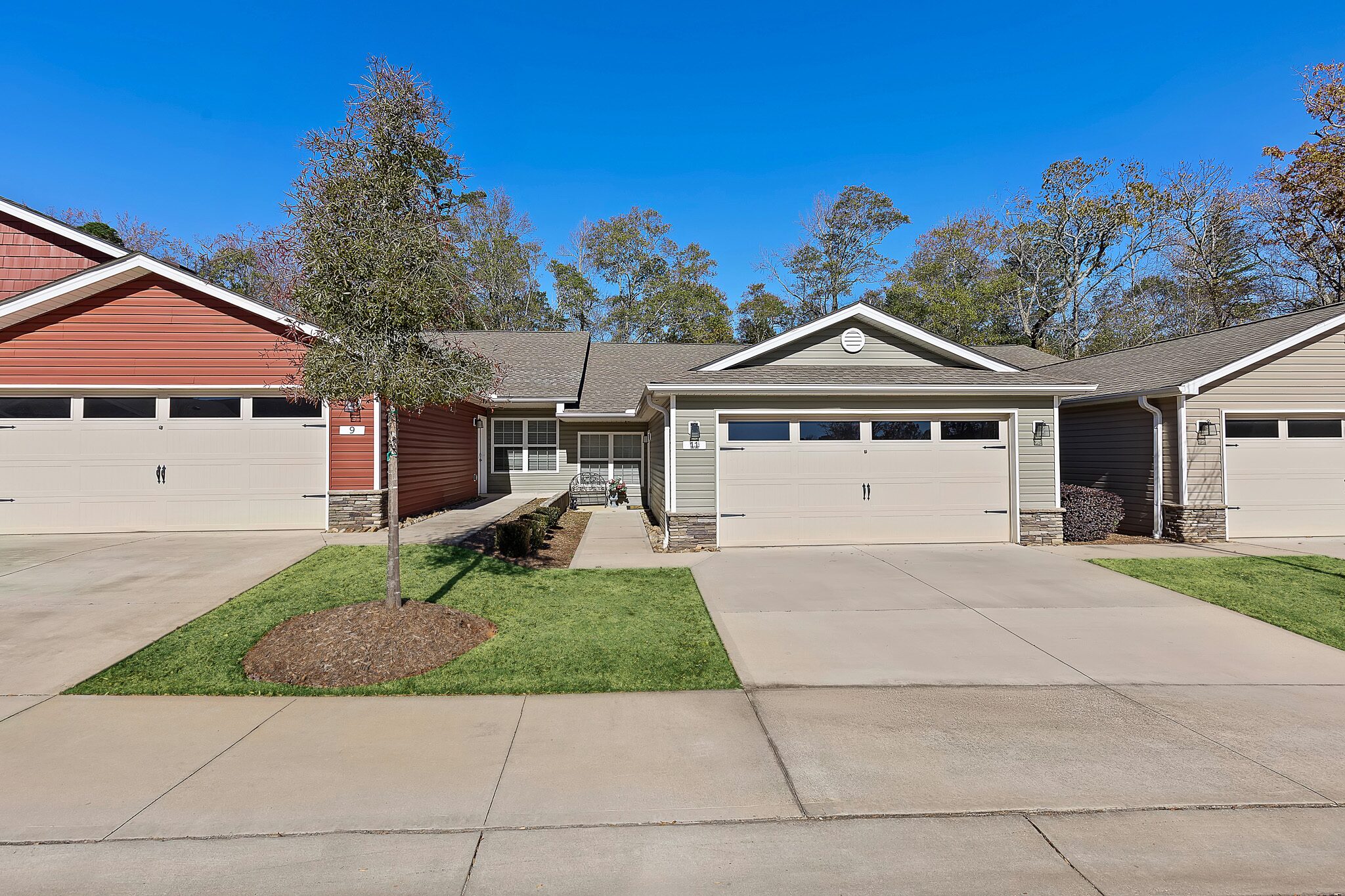 Single-story suburban house with beige siding, a double garage, and a small front yard, situated between two similar houses on a sunny day.